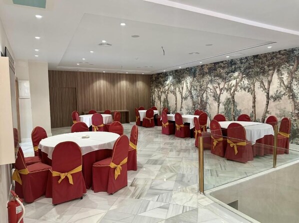 A conference room with round tables and red chairs, a marble floor, and a mural of trees on the wall.