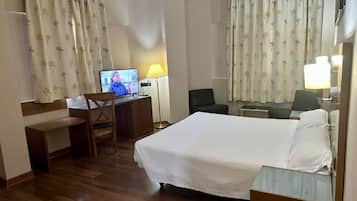 Una habitación de hotel con una cama, un escritorio con computadora, una silla y una lámpara.