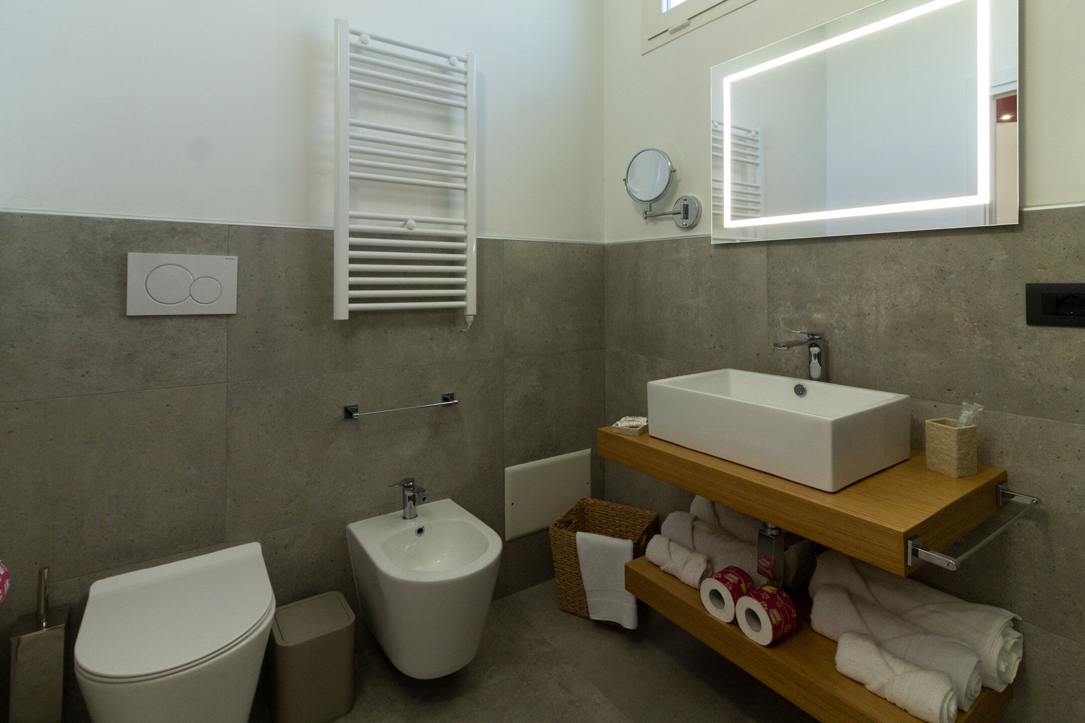 A modern bathroom with a toilet, bidet, and a large mirror above the sink.