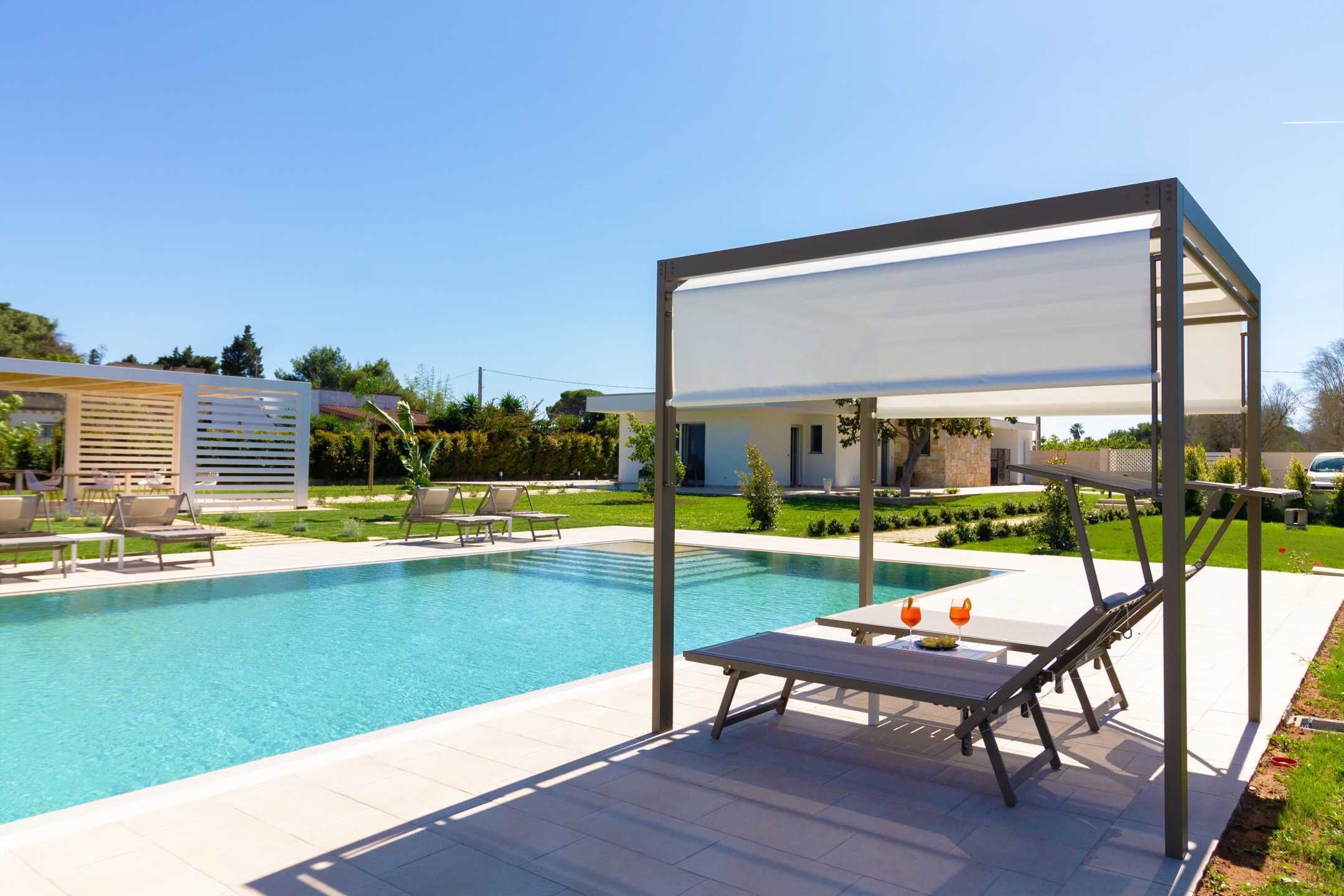 Un área de piscina moderna al aire libre con sillones de descanso y una zona de estar cubierta.