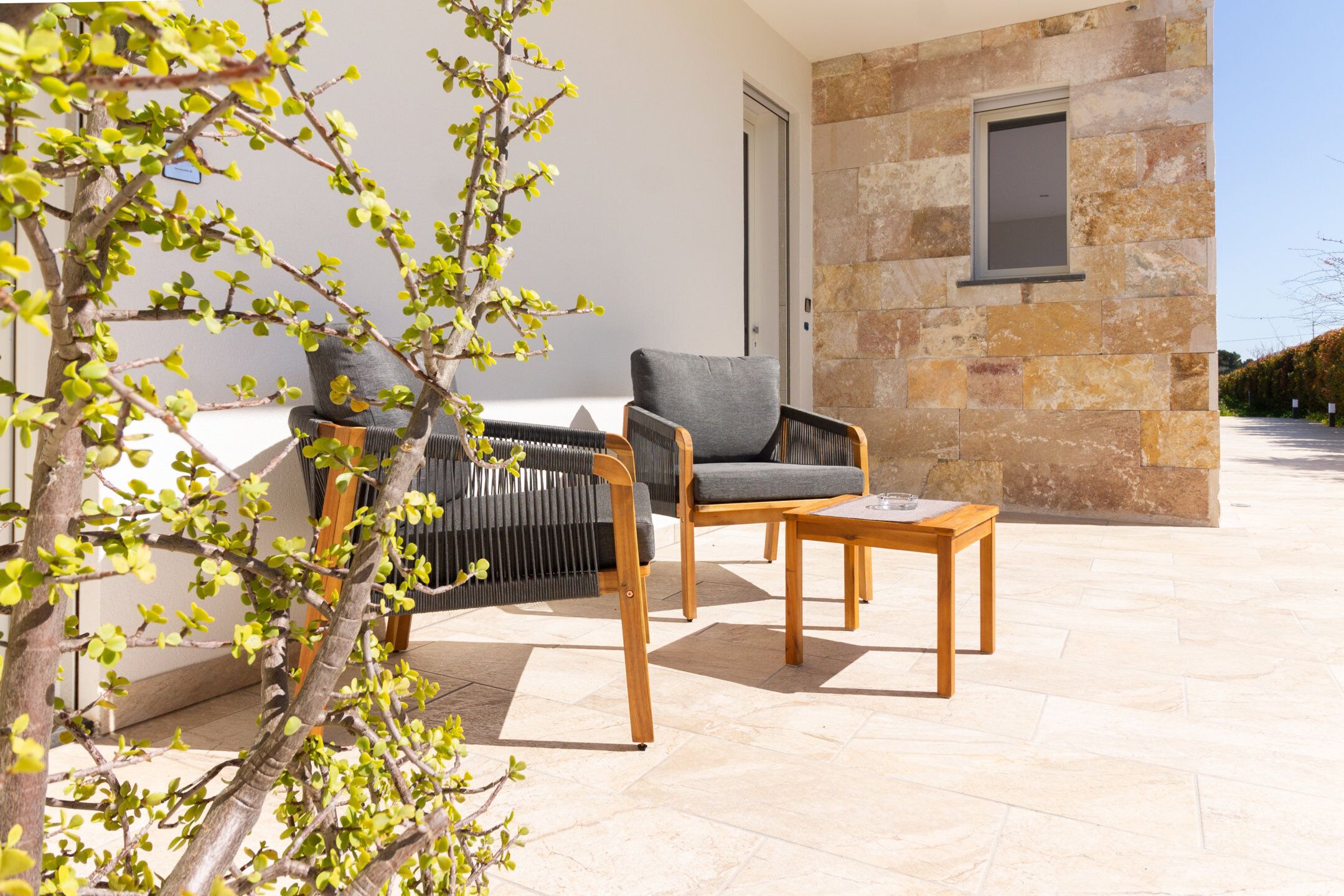 A patio with a stone wall, a wooden table, and two chairs.