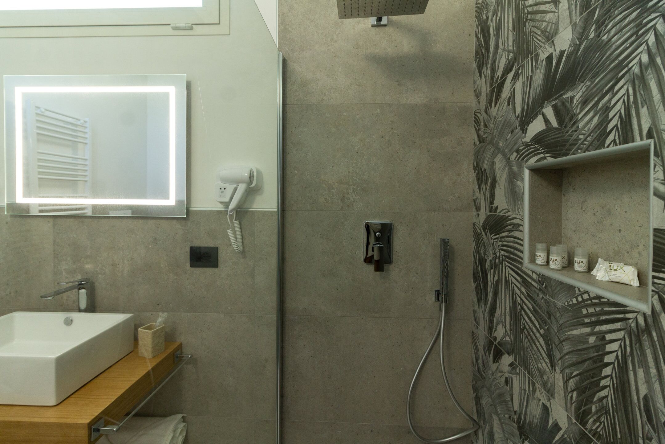 A bathroom with a rectangular sink, a mirror, a hairdryer, and a shower area with a palm leaf wall design.