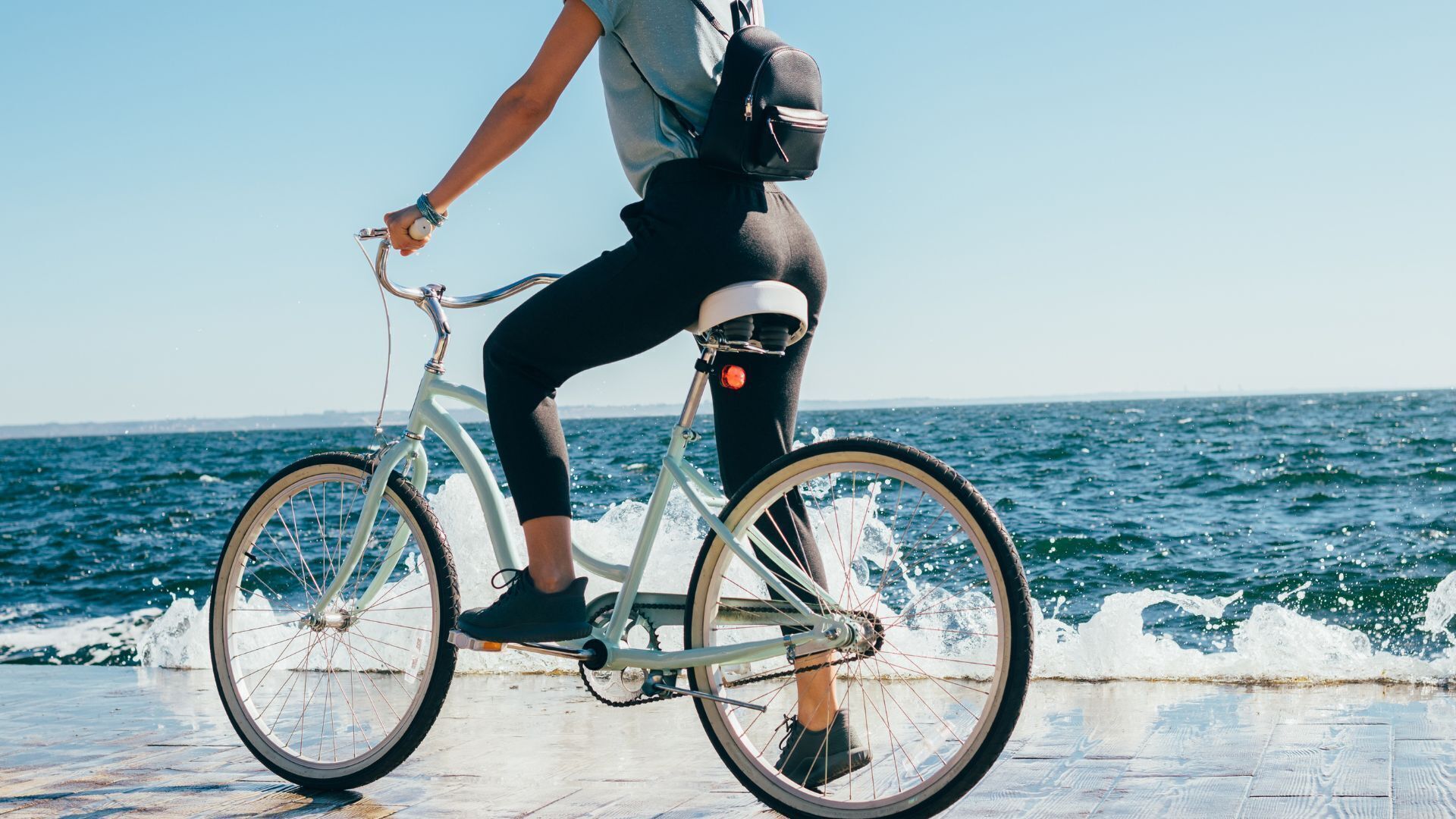 A person riding a bicycle on a paved path by the sea.