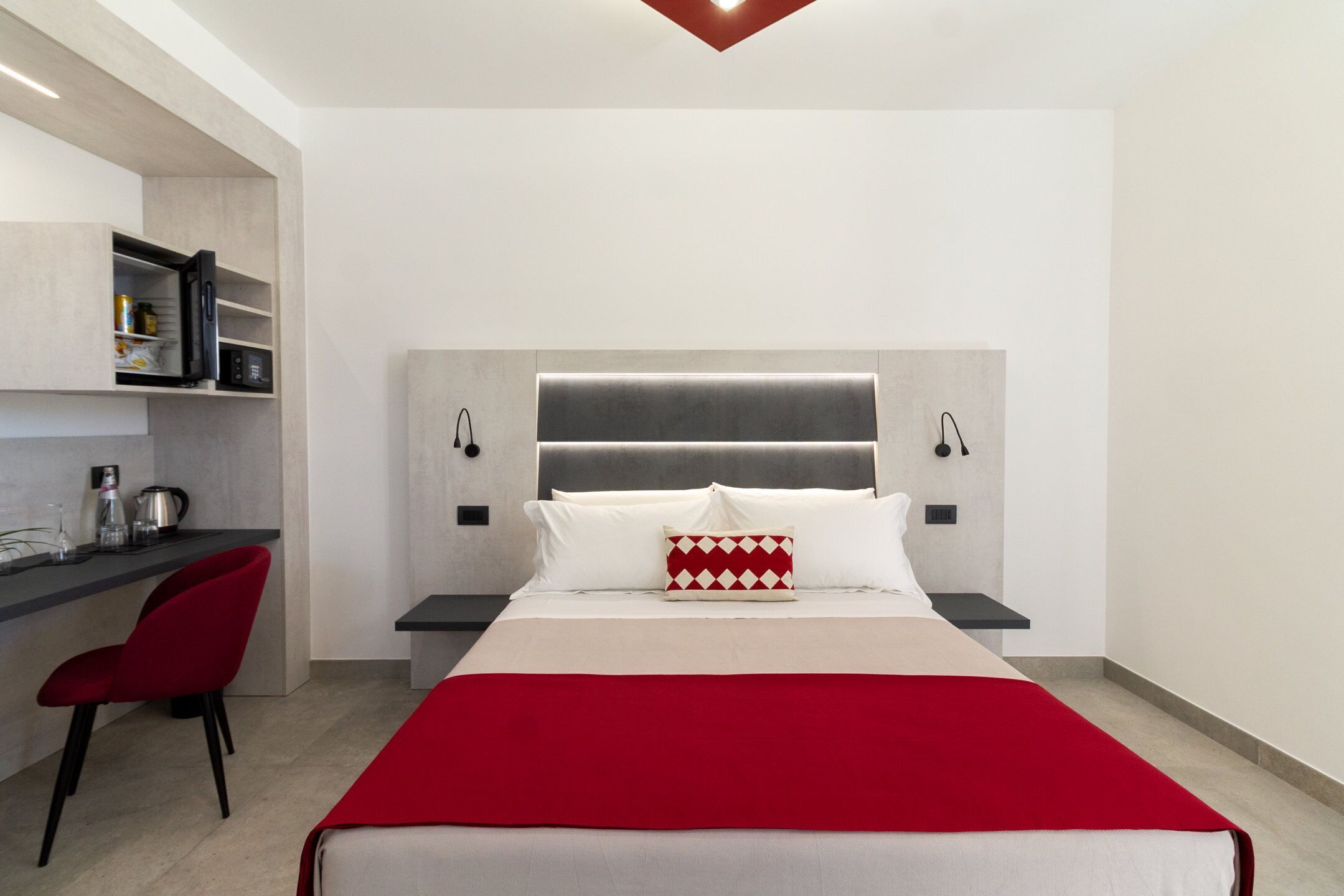 Une chambre moderne avec un lit, un fauteuil rouge, un bureau et un coin cuisine.