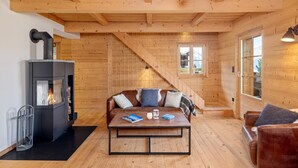 A cozy cabin interior with a wooden interior, a fireplace, a sofa, and a table with books and a mug. - Chalet Les Aragnes Family Chalet La Tzoumaz (Riddes)