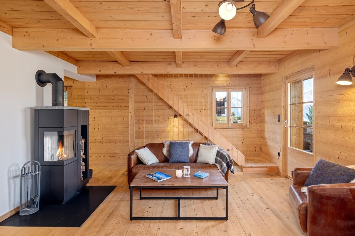 A cozy cabin interior with a wooden interior, a fireplace, a sofa, and a table with books and a mug.