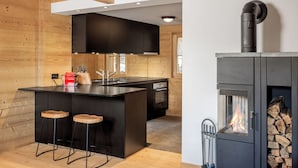 Une cuisine moderne dotée d’un îlot central, de meubles de rangement noirs et d’un poêle à bois.
