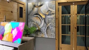 Een moderne kantoorruimte met een bureaucomputer, een groot abstract schilderij en houten deuren.
