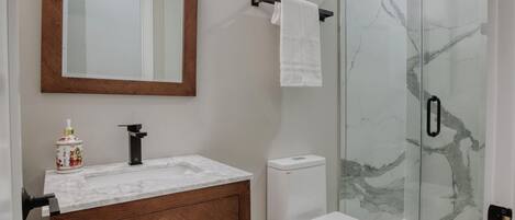 A modern bathroom with a marble sink, wooden vanity, white toilet, and a glass shower enclosure.