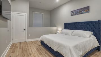 A bedroom with a large bed, a cityscape painting, and a window with blinds.