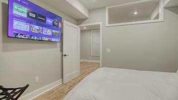 A bedroom with a bed, a TV mounted on the wall displaying various channels, and a door leading to another room.