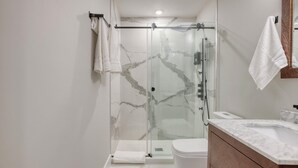 A modern bathroom with a glass-enclosed shower, a white toilet, and a marble countertop sink.