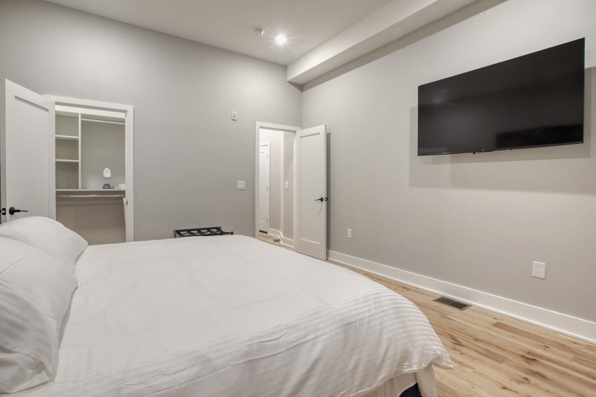 Een slaapkamer met een groot bed, een garderobe, een spiegel en een flatscreen televisie aan de muur.