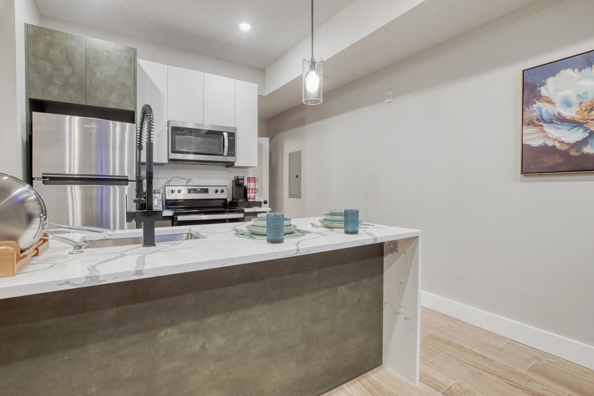 A modern kitchen with stainless steel appliances, a marble countertop, and a pendant light.