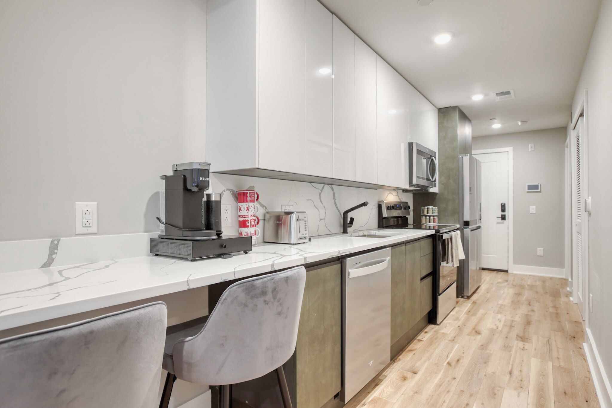 A modern kitchen with white cabinets, a marble countertop, a coffee maker, a toaster, and a microwave.