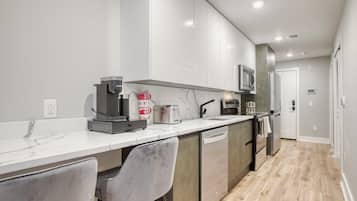 A modern kitchen with white cabinets, a marble countertop, a coffee maker, a toaster, and a microwave.