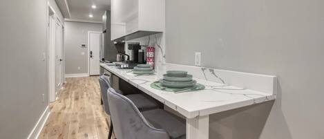 A modern kitchen with a white countertop, grey chairs, and a wooden floor.