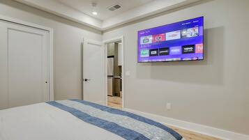 A bedroom with a large bed, a flat-screen TV mounted on the wall displaying various streaming services, and a door leading to a hallway.