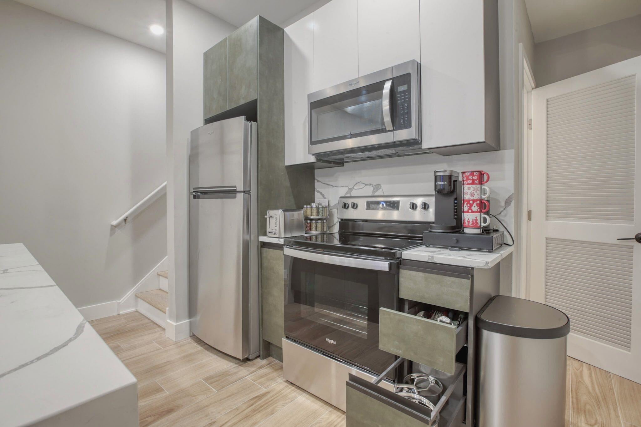 A modern kitchen with stainless steel appliances, a microwave, a coffee maker, and a trash can.
