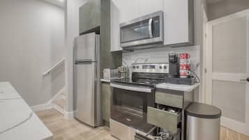 A modern kitchen with stainless steel appliances, a microwave, a coffee maker, and a trash can.