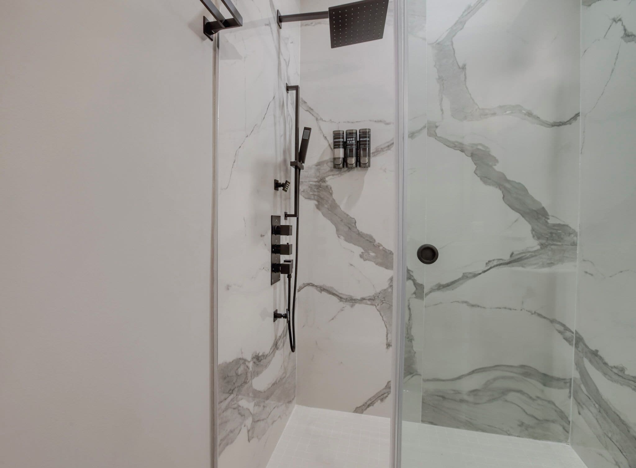 A modern shower with a glass door, marble walls, and a handheld showerhead.