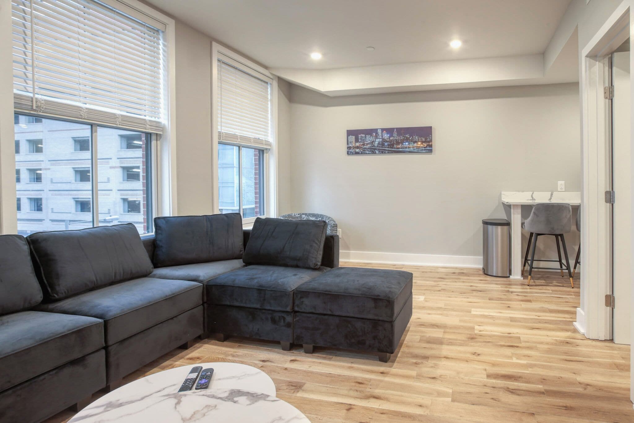 A modern living room with a sectional sofa, a small table, and a cityscape painting on the wall.