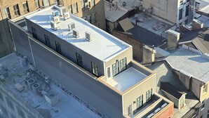 A multi-story building with a flat roof, several air conditioning units, and a mix of brick and modern architectural styles.