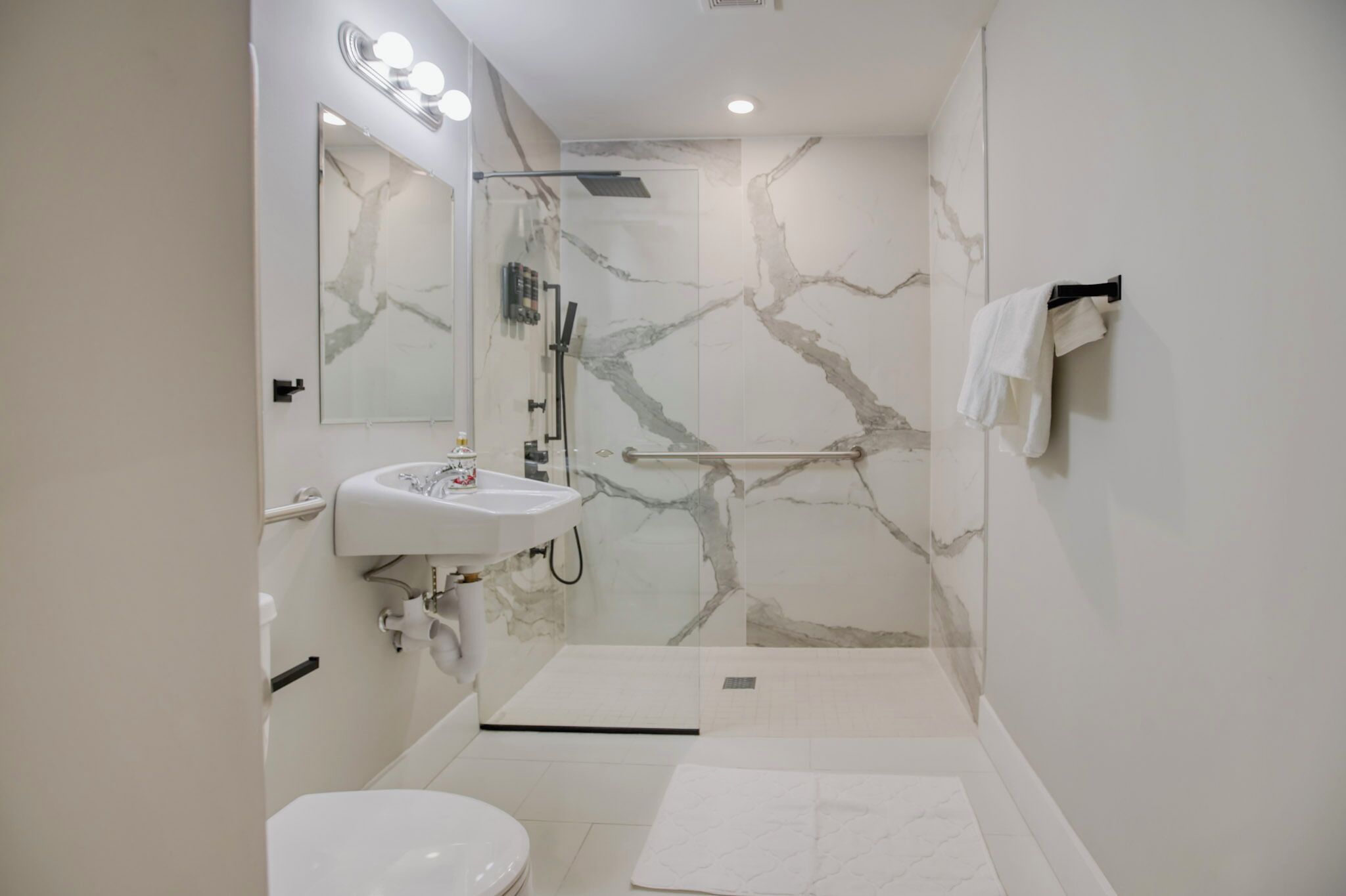 A modern bathroom with a marble shower wall, a white sink, and a toilet.