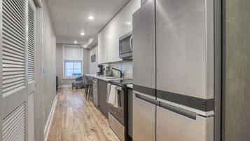 A modern kitchen with stainless steel appliances, a window with blinds, and a wooden floor.
