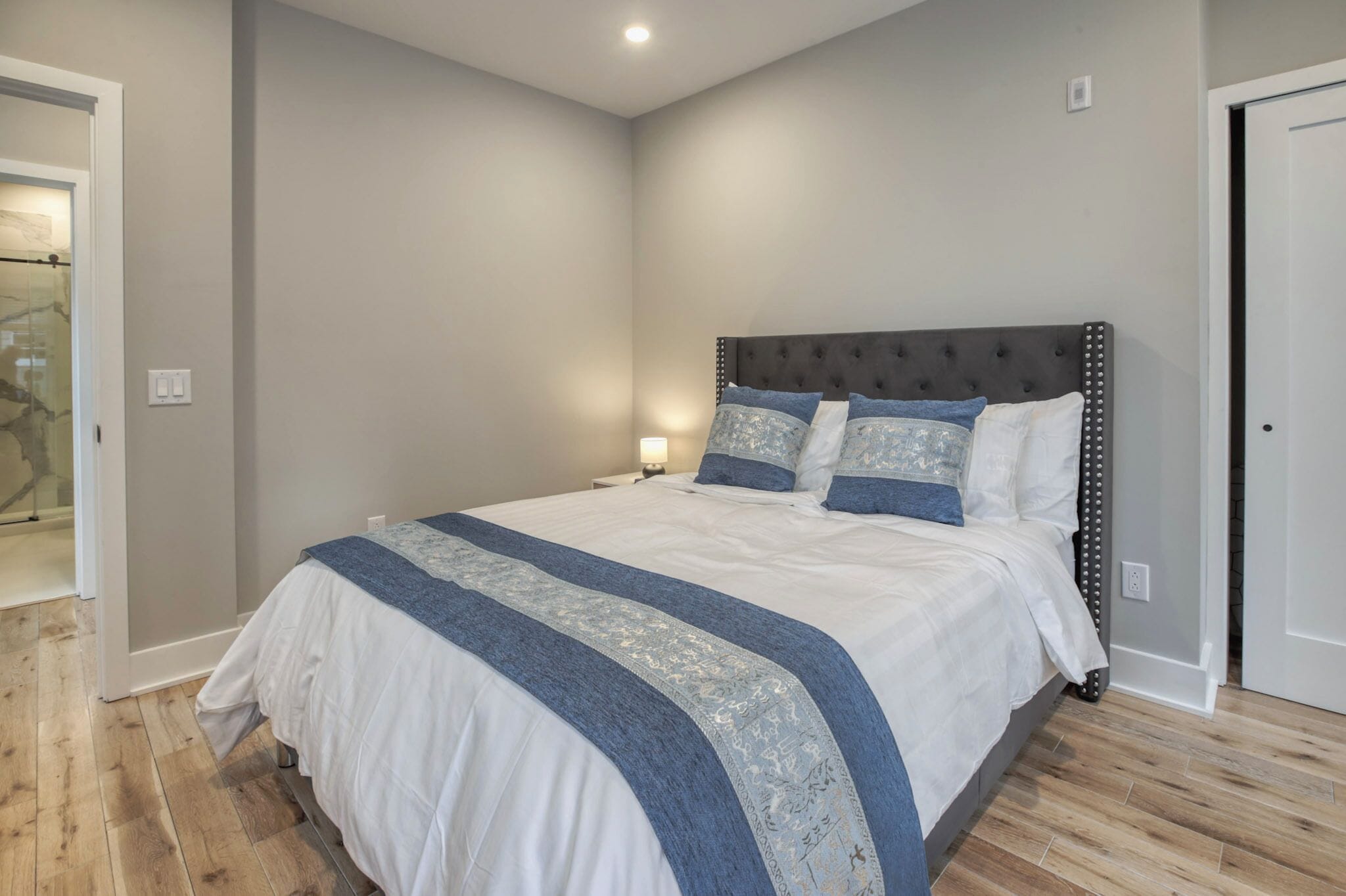 A bedroom with a large bed, a nightstand, and a wall-mounted lamp.