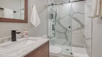 Een moderne badkamer met een marmeren wastafel, een douche met glazen wanden en een toilet.