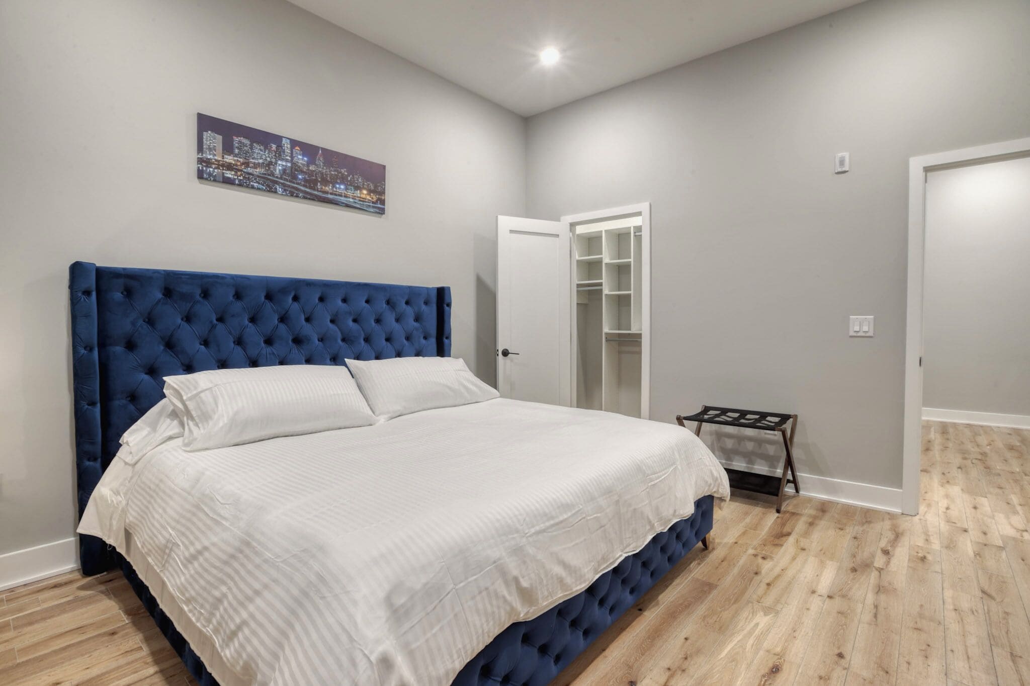 A bedroom with a large bed, a wardrobe, and a cityscape painting on the wall.