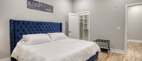 A bedroom with a large bed, a wardrobe, and a cityscape painting on the wall.