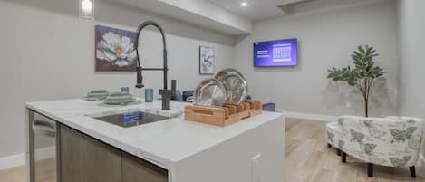 A modern kitchen with a central island, stainless steel appliances, and a digital screen displaying a menu.