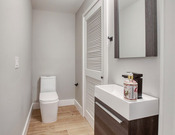 A small bathroom with a toilet, a sink with a mirror, and a bottle of hand soap. - One Sky Loft (Philadelphia)