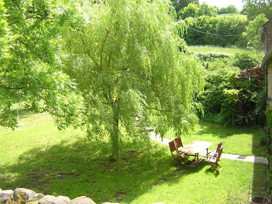 En frodig grøn have med et træ, en stenvæg samt et træbord og stole.