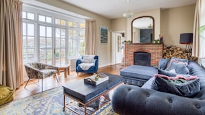 A living room with a fireplace, a blue armchair, a patterned armchair, a coffee table, and a large sofa with pillows.