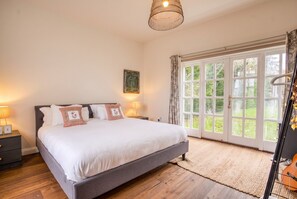 A bedroom with a large bed, a nightstand, a lamp, and a view of the outdoors through a window.
