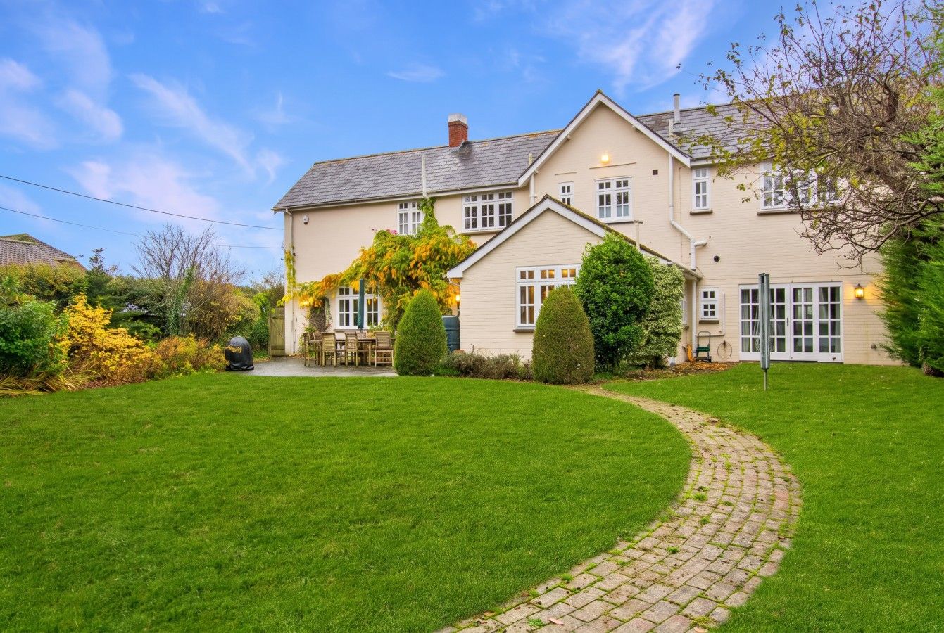 A two-story house with a paved driveway leading to the front door, surrounded by a well-maintained lawn and various shrubs.