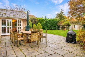 A patio with a table and chairs, a grill, and a house in the background. - Spacious 5-bedroom home with cinema room, Aga kitchen & forest walks (East Boldre)