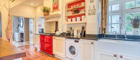 A kitchen with white cabinets, a red stove, a washing machine, and a window with curtains.