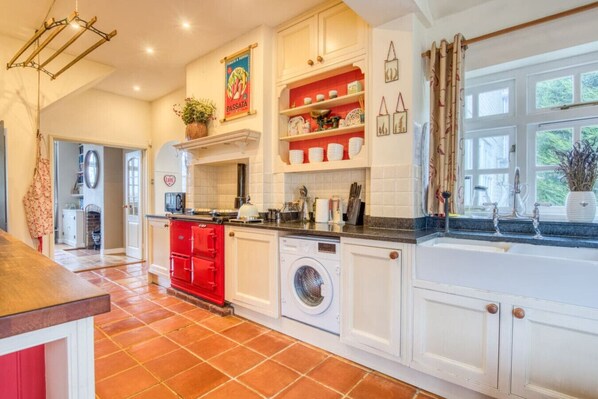A kitchen with white cabinets, a red stove, a washing machine, and a window with curtains.