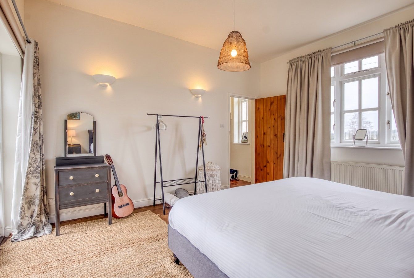 Un dormitorio con una cama, un aparador, una guitarra, una lámpara colgante y una ventana con cortinas.