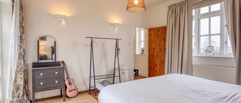 Un dormitorio con una cama, un aparador, una guitarra, una lámpara colgante y una ventana con cortinas.