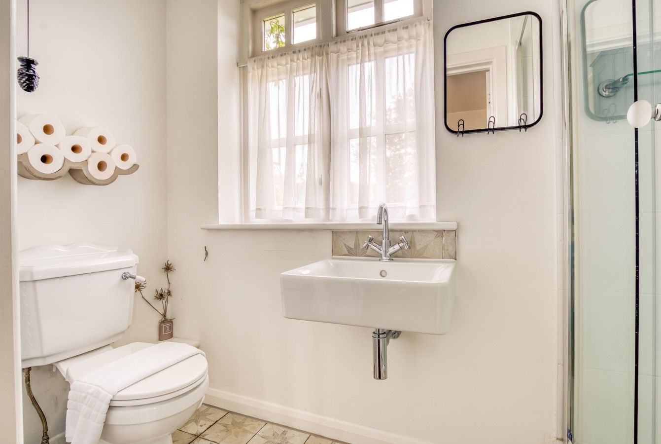 A bathroom with a toilet, sink, and window with curtains.