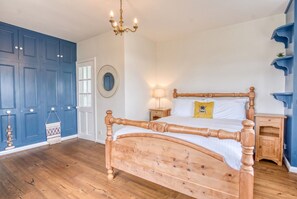 A bedroom with a wooden bed, a nightstand, a lamp, and a blue door. - Spacious 5-bedroom home with cinema room, Aga kitchen & forest walks (East Boldre)
