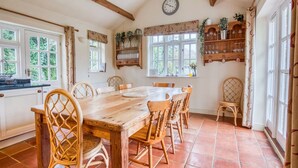 A dining area with a wooden table and chairs, a clock on the wall, and a window with curtains.