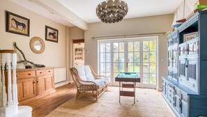 A spacious room with a wooden cabinet, a wicker chair, a billiards table, and a large window with a view of greenery.