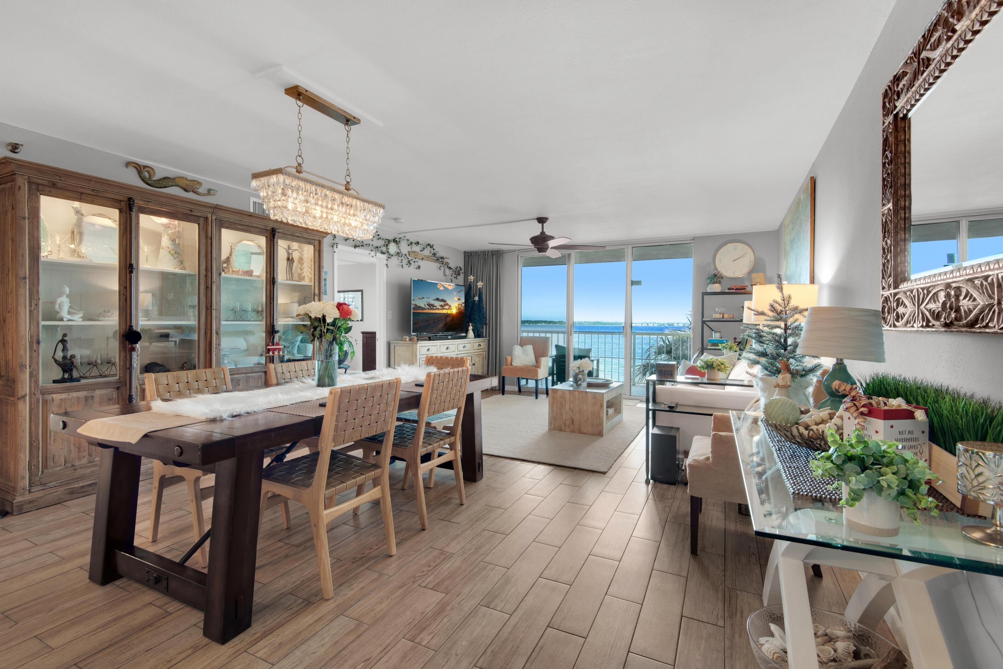 A spacious living area with a large dining table, wooden chairs, a chandelier, and a view of the ocean through large windows.
