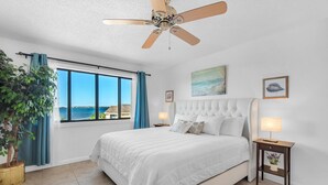 Un dormitorio con una cama grande, ventilador de techo, vista al mar y una planta en maceta.